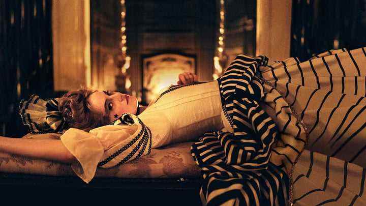 Emma Stone, The Favourite'da bir şöminenin önüne uzanır.