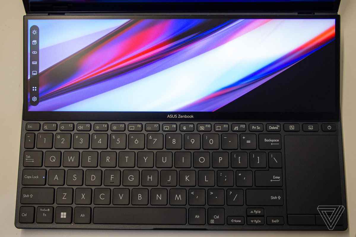 Asus Zenbook Pro Duo 14'ün klavye güvertesi yukarıdan görülüyor.  ScreenPad, sol tarafında bir görev çubuğu bulunan çok renkli bir arka plan görüntüler.