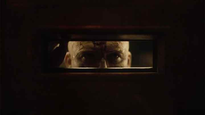Men'den bir sahnede Rory Kinnear'ın karakteri bir kapının posta deliğinden bakıyor.