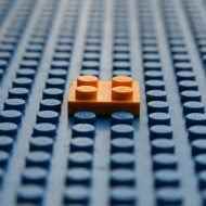 Büyük, boş bir LEGO plakasının üzerinde duran turuncu bir LEGO tuğlası