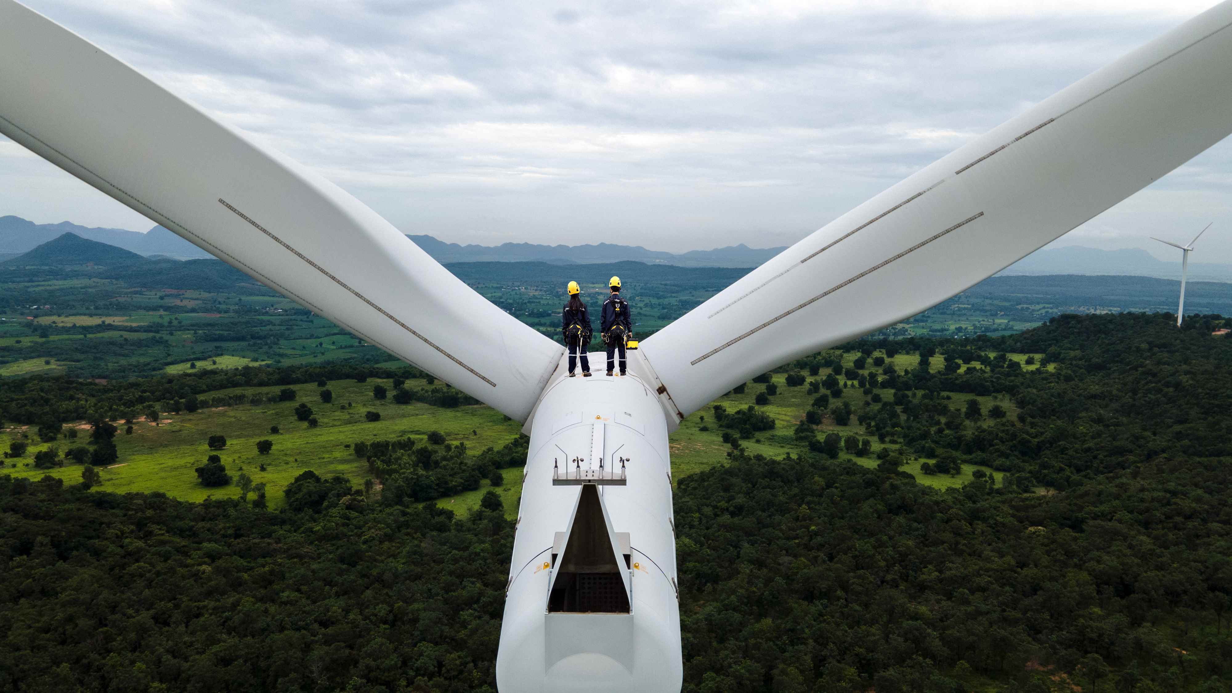 Rüzgar türbini çiftliğinin tepesinde çalışan Kişisel koruyucu ekipman giyen iki Elektrik mühendisi;  iklim teknolojisi yatırımcı anketi