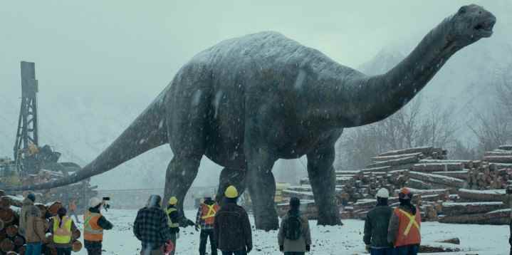 Jurassic World Dominion'dan bir sahnede büyük bir dinozor bir şantiyede yürüyor.