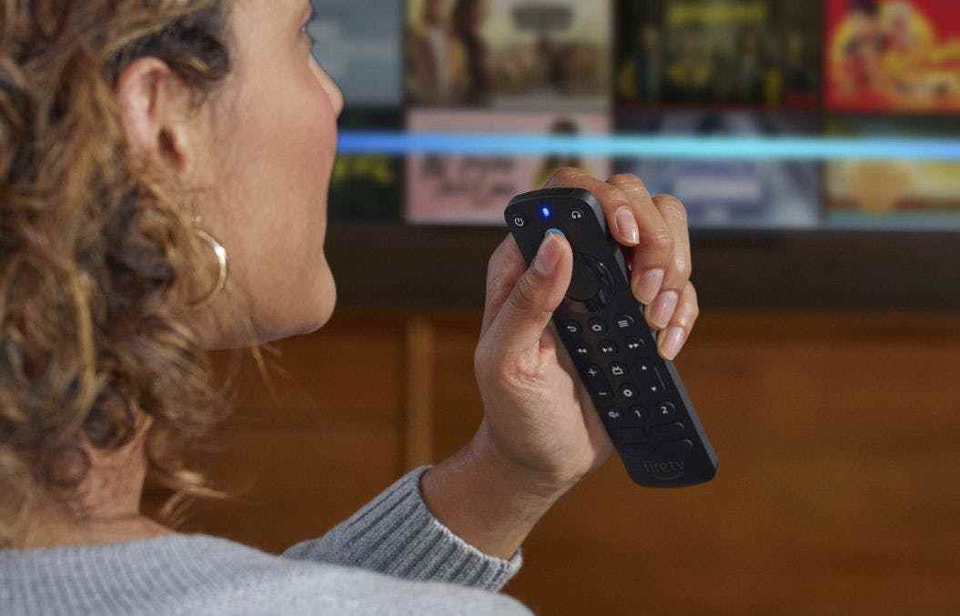 Amazon'un Alexa Voice Remote Pro'suna sol elinde tutarken sesli komutlar veren bir kadının görüntüsü.