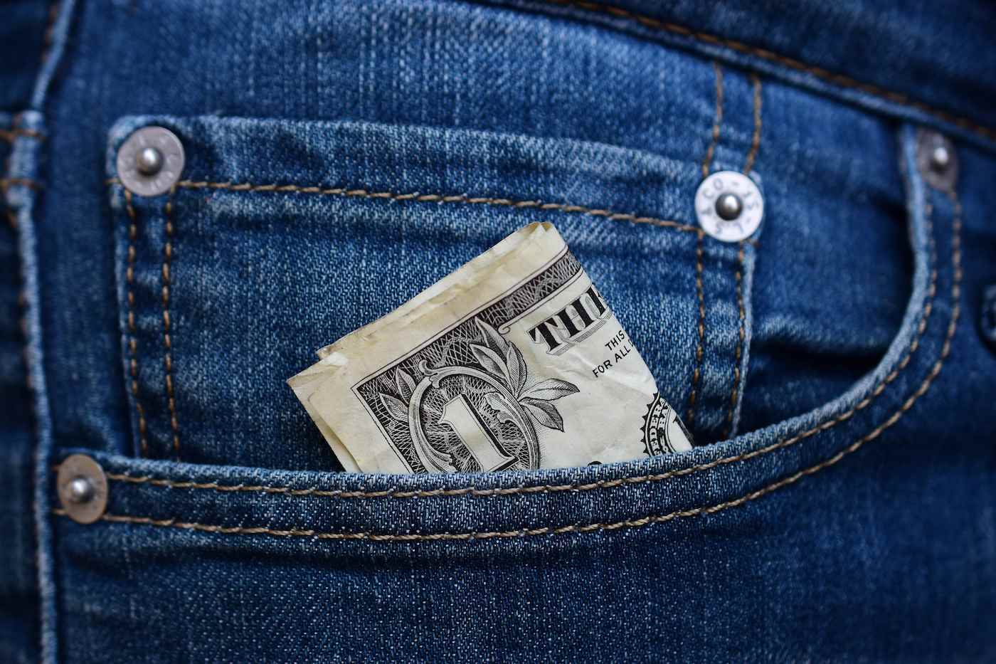 Bir kot pantolonun ön cebine sıkıştırılmış, katlanmış bir dolarlık banknot.