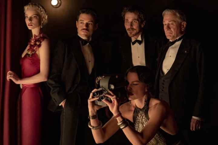 Margot Robbie, Amsterdam'da Anya Taylor-Joy, Rami Malek, Christian Bale ve Robert De Niro'nun önünde çömelmiş bir film kamerası tutuyor.