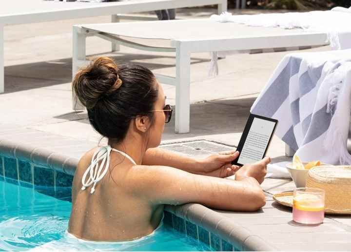 Yüzme havuzundayken Amazon Kindle Oasis'te e-kitap okuyan bir kadın.