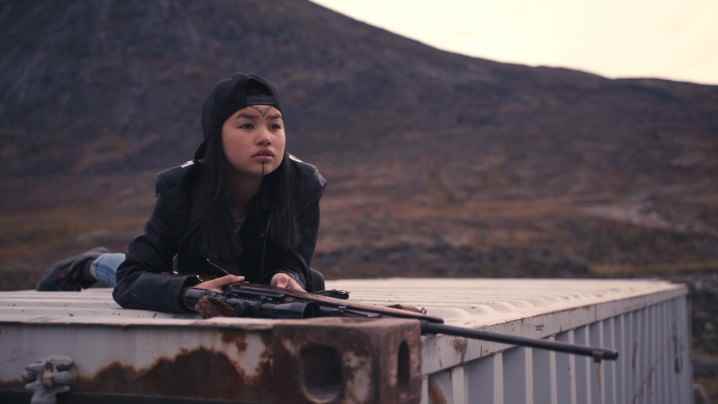Slash/Back filminden bir sahnede Tasiana Shirley elinde tüfek olan bir nakliye konteynerinin üzerinde oturuyor.