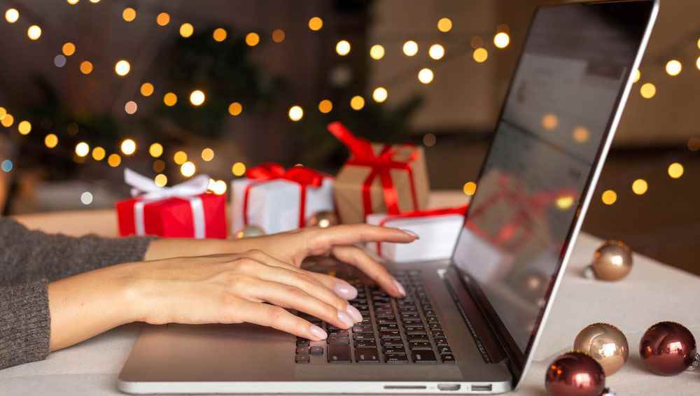 Kadının elleri, her yerde Noel ağacı ve tatil süslemeleriyle MacBook'a yazıyor.
