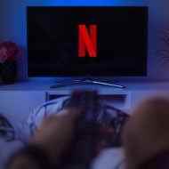 Netflix logosunu gösteren bir TV'nin bir kişi tarafından izlendiği fotoğrafı