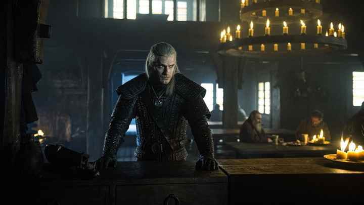 Geralt, The Witcher'da elleri masanın üzerinde ciddi görünüyor.