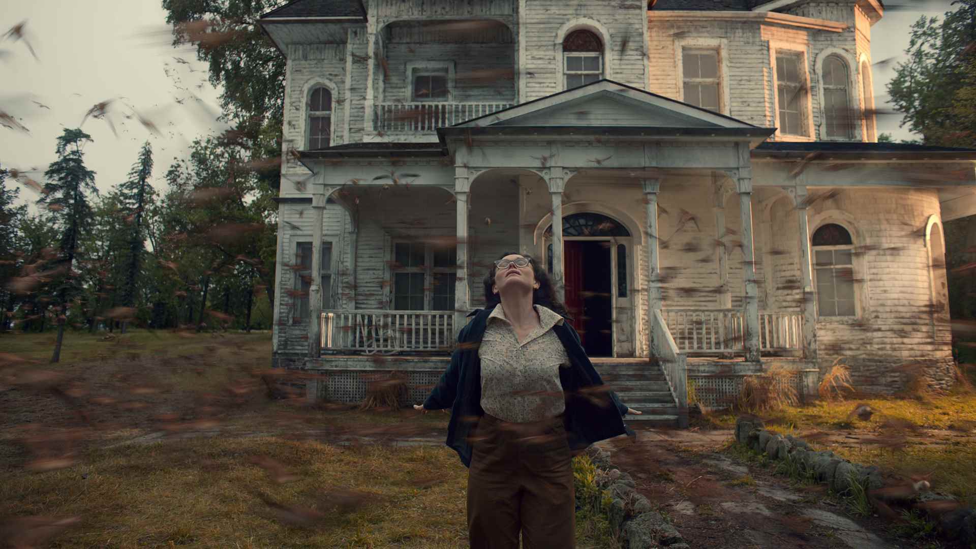 Netflix'teki The Murmuring'de Nancy Bradley, şiddetli bir rüzgar ona çarparken bir evin önünde duruyor