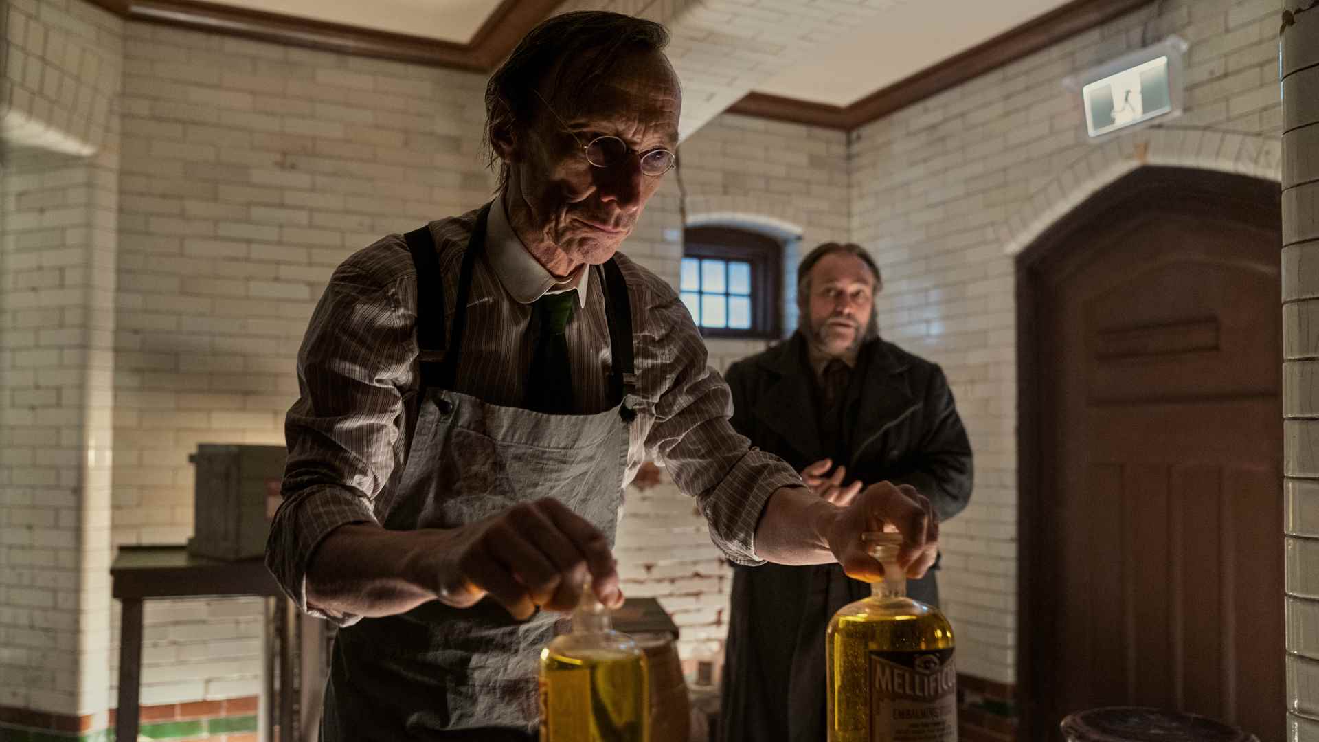 Netflix'teki Graveyard Rats'ta bir bilim adamı iki kavanoz tutuyor ve Masson arkasında duruyor
