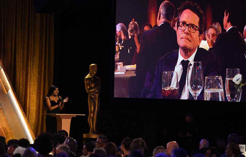 Aktris Mindy Kaling, 19 Kasım 2022'de Los Angeles'taki Fairmont Century Plaza'da düzenlenen Sinema Sanatları ve Bilimleri Akademisi'nin 13. Yıllık Valiler Ödülleri'nde ekrana gelen Kanadalı-Amerikalı aktör Michael J. Fox'u canlandırırken konuşuyor.