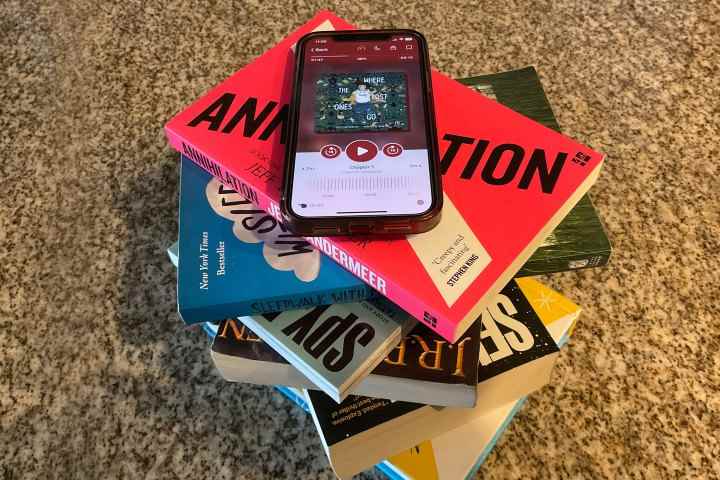 Çeşitli kitaplardan oluşan bir kulenin tepesinde oturan bir iPhone 12'de görüntülenen Libby uygulaması.