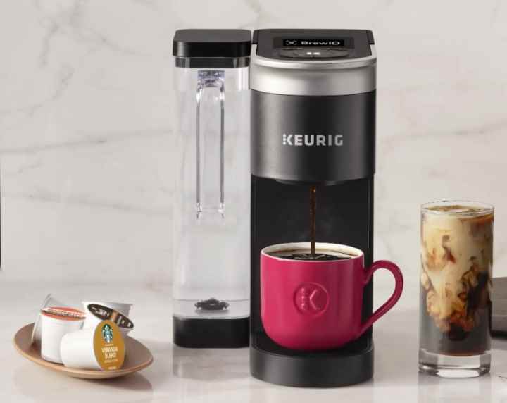 Bir Keurig K-Supreme kahve makinesi, mutfak tezgahında K-Cup'ların ve bir bardak buzlu kahvenin yanında duruyor.