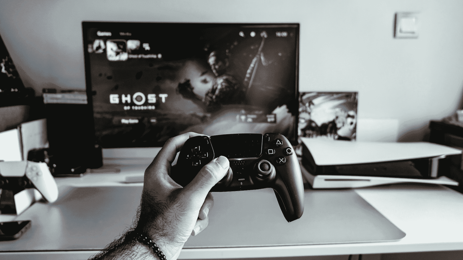 Ghost of Tsushima'yı gösteren bir TV'nin önünde siyah PS5 DualSense denetleyicisini tutan adamın eli