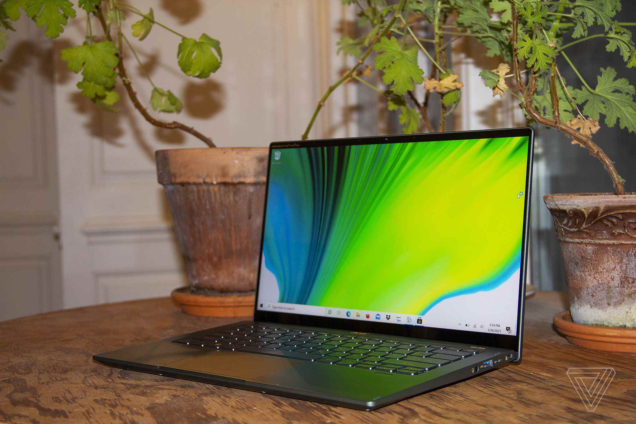 Acer Swift 5, iki ev bitkisinin önünde bir masa üzerinde, açık ve sola açılı.  Ekranda yeşil, mavi ve beyaz bir arka plan görüntülenir.