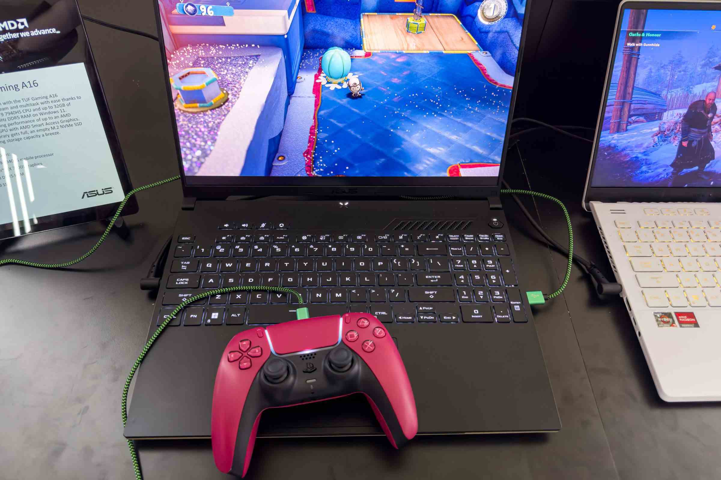 Asus TUF Gaming A16 klavye, dokunmatik yüzey üzerinde duran kırmızı bir PS5 kontrolcüsü ile yukarıdan görülüyor.