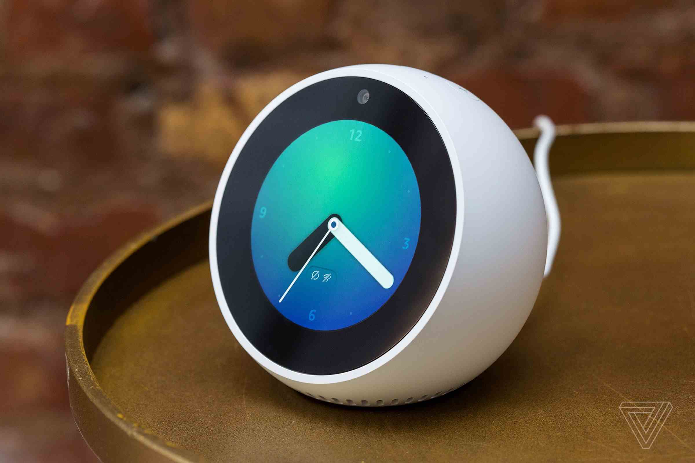 Masanın üzerinde oturan yuvarlak saat görünümlü yarım eldiven olan Amazon Echo Spot'un 2017 versiyonu.