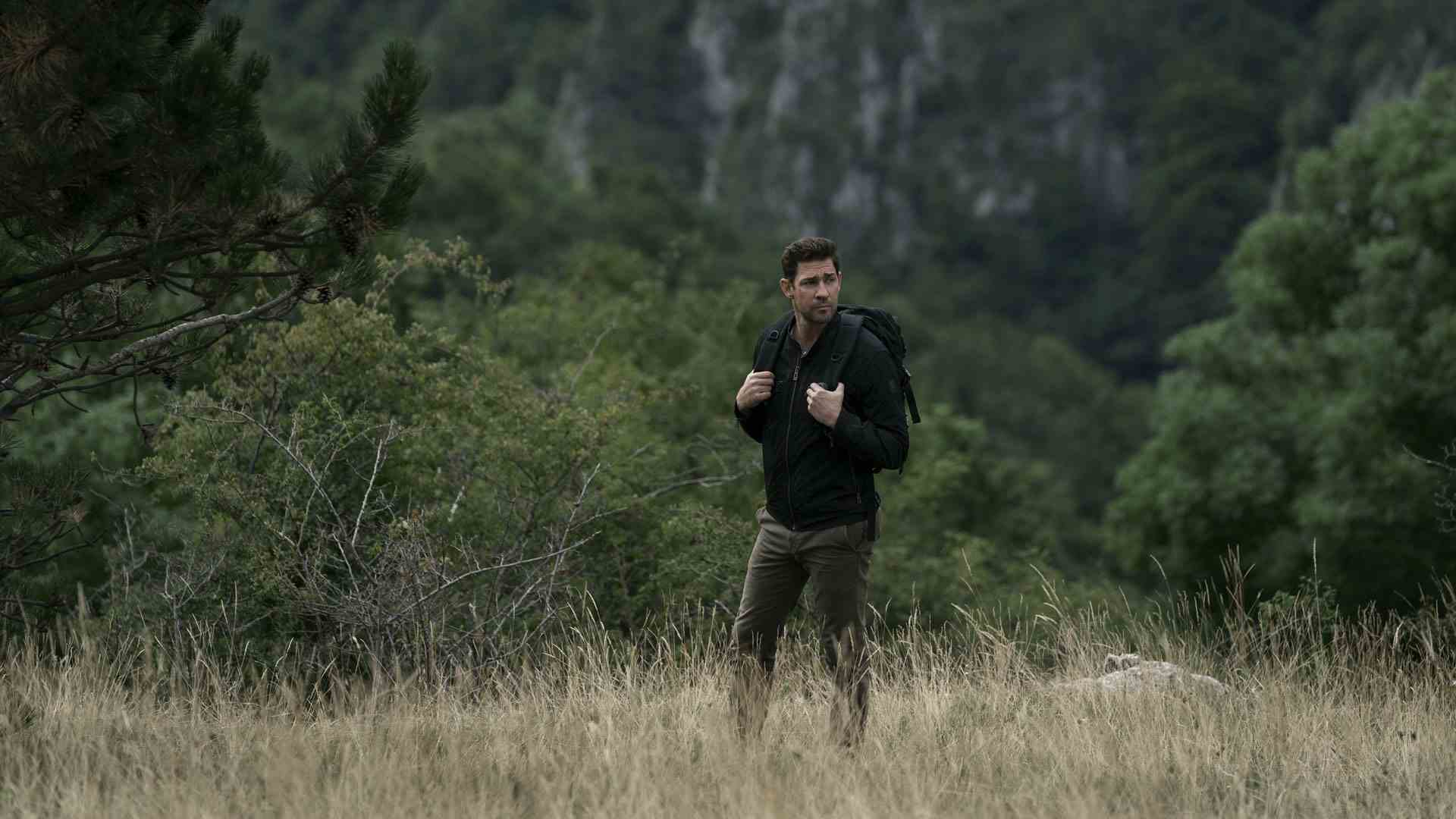 Jack Ryan, Tom Clancy'nin Jack Ryan 3. sezonunda sırt çantasıyla açık bir alanda yürüyor.