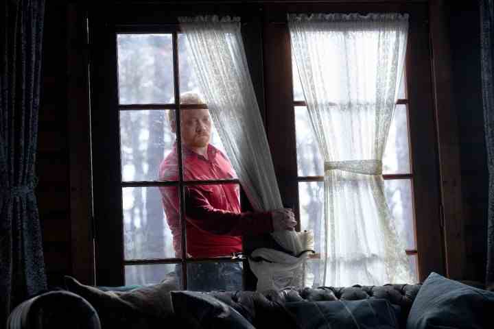 Rupert Grint, Knock at the Cabin'den bir sahnede elini kırık bir kapıdan içeri sokuyor.