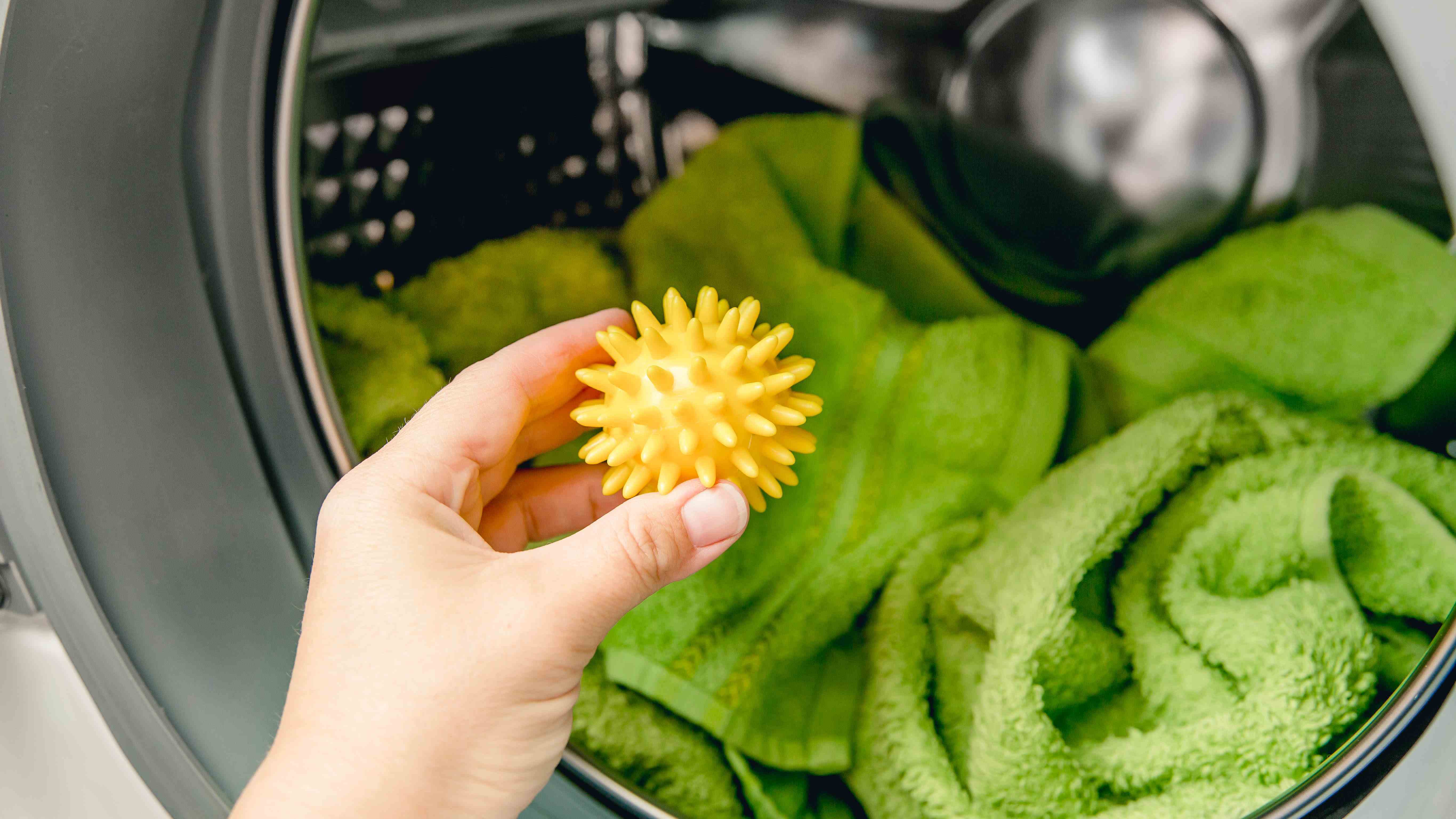 Yeşil havlularla dolu bir çamaşır kurutma makinesine kauçuk sarı bir kurutma topu ekleniyor