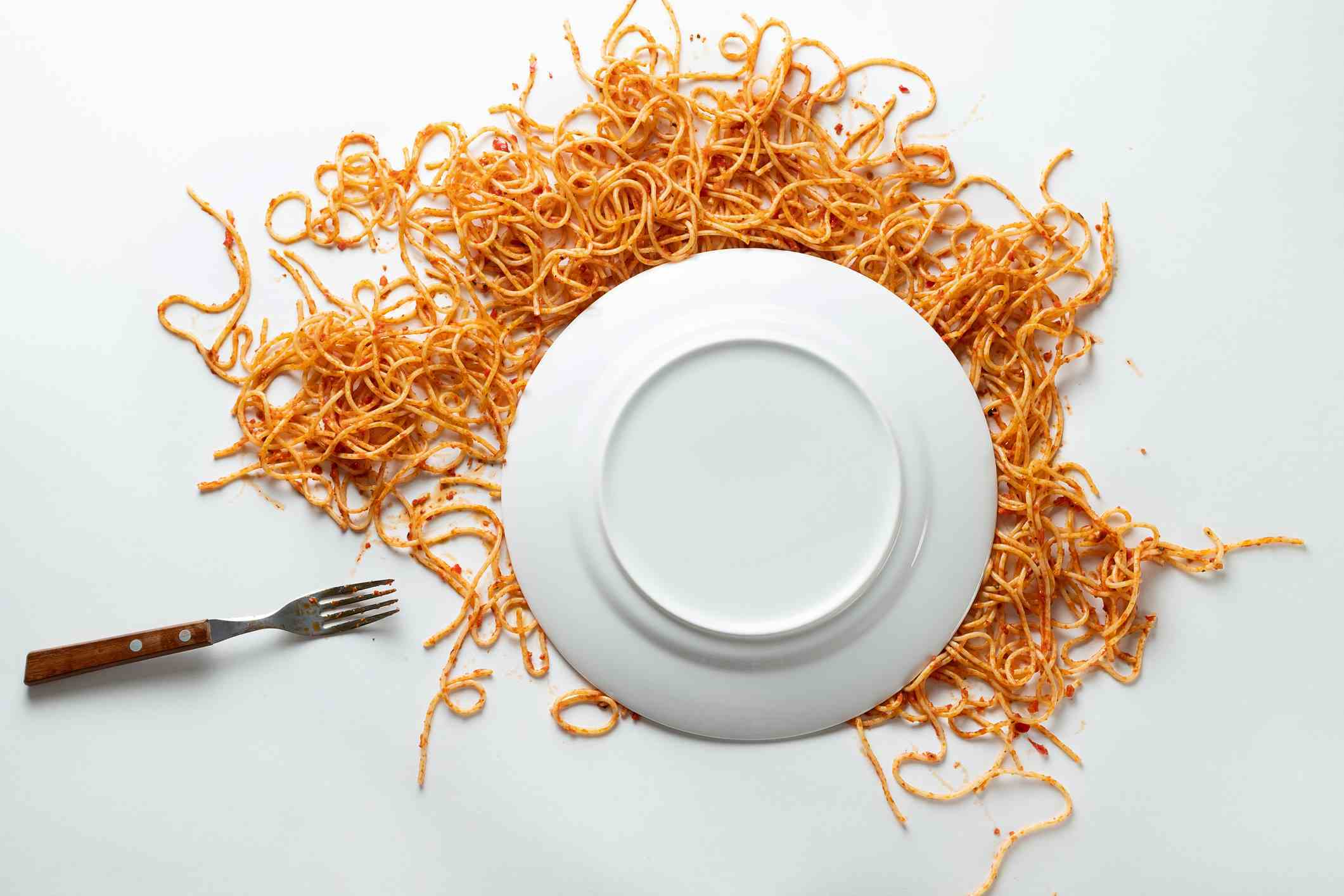 Yanında çatal olan, düşmüş beyaz seramik spagetti tabağı.  Domates soslu makarna bolonez beyaz bir arka plana veya masaya dağılmıştır.  Vejetaryen ve vegan gıda kavramı.  Gıda geçmişi.  Metin alanının kopyası.