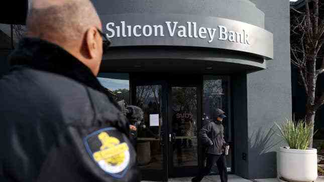 Bir güvenlik görevlisi, bir müşterinin 13 Mart 2023'te Santa Clara, California'da bir Silicon Valley Bank ofisinden çıkışını izliyor.  Silikon Vadisi Bankası çöktükten günler sonra, müşteriler iflas eden bankadan fonlarını geri almak için sıraya giriyor.  Silikon Vadisi Bankası başarısızlığı, ABD tarihindeki en büyük ikinci başarısızlıktır.