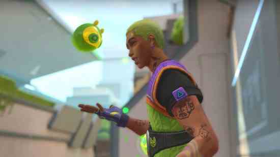 Neon yeşili ve mor taktik yelek giyen parlak neon yeşili saçlı bir Latin adam, sarı süper kahraman tarzı maskeli küçük yeşil bir balçık ona tepeden bakarken elini uzatıyor.