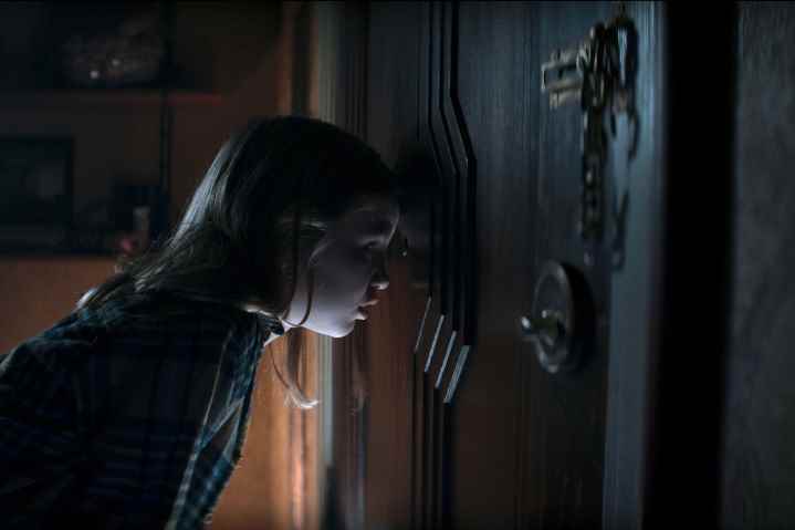 Kassie, Evil Dead Rise'da bir kapının gözetleme deliğinden bakıyor.