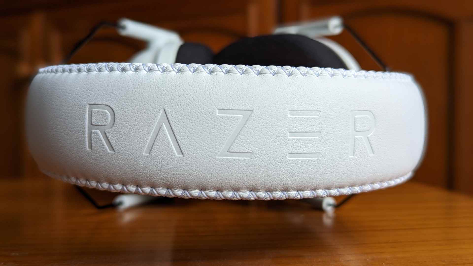 Razer BlackShark V2 Pro incelemesi: Ahşap bir yüzeyin üzerinde oturan kablosuz bir oyun kulaklığı.  Kafa bandına 'RAZER' yazısı işlenmiştir.