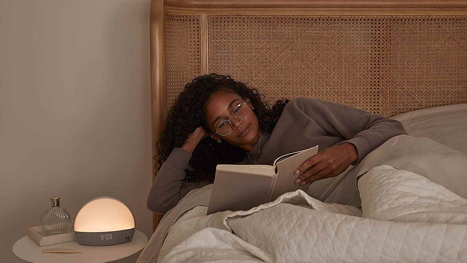 Kıvırcık siyah saçlı bir kadın uyumadan önce rahatlamak için yatakta kitap okuyor.