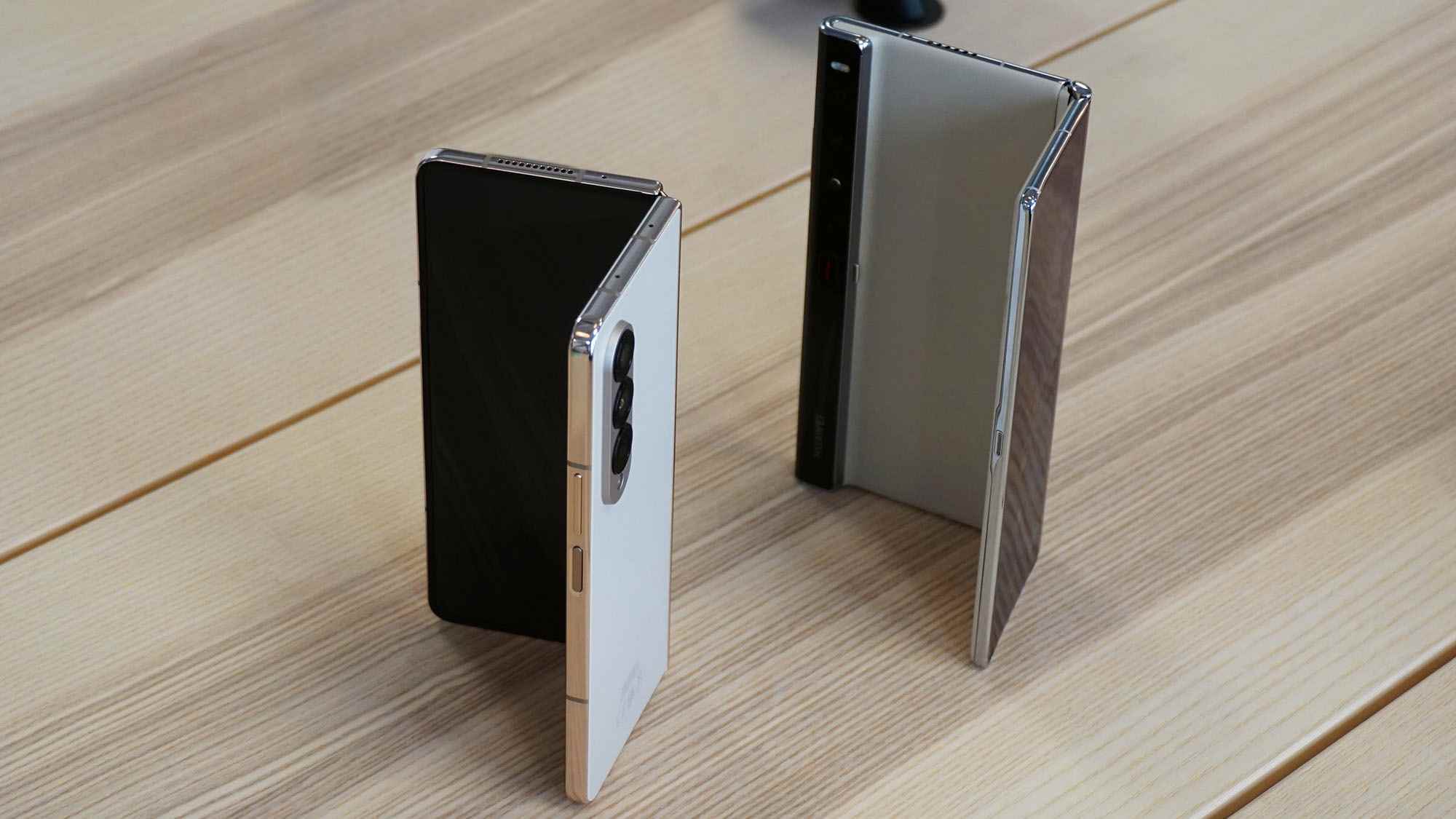 Kısmen katlanmış bir Huawei Mate Xs 2'nin yanında kısmen katlanmış bir Samsung Galaxy Z Fold 4, her ikisi de çıplak bir çam masasının üzerinde duruyor