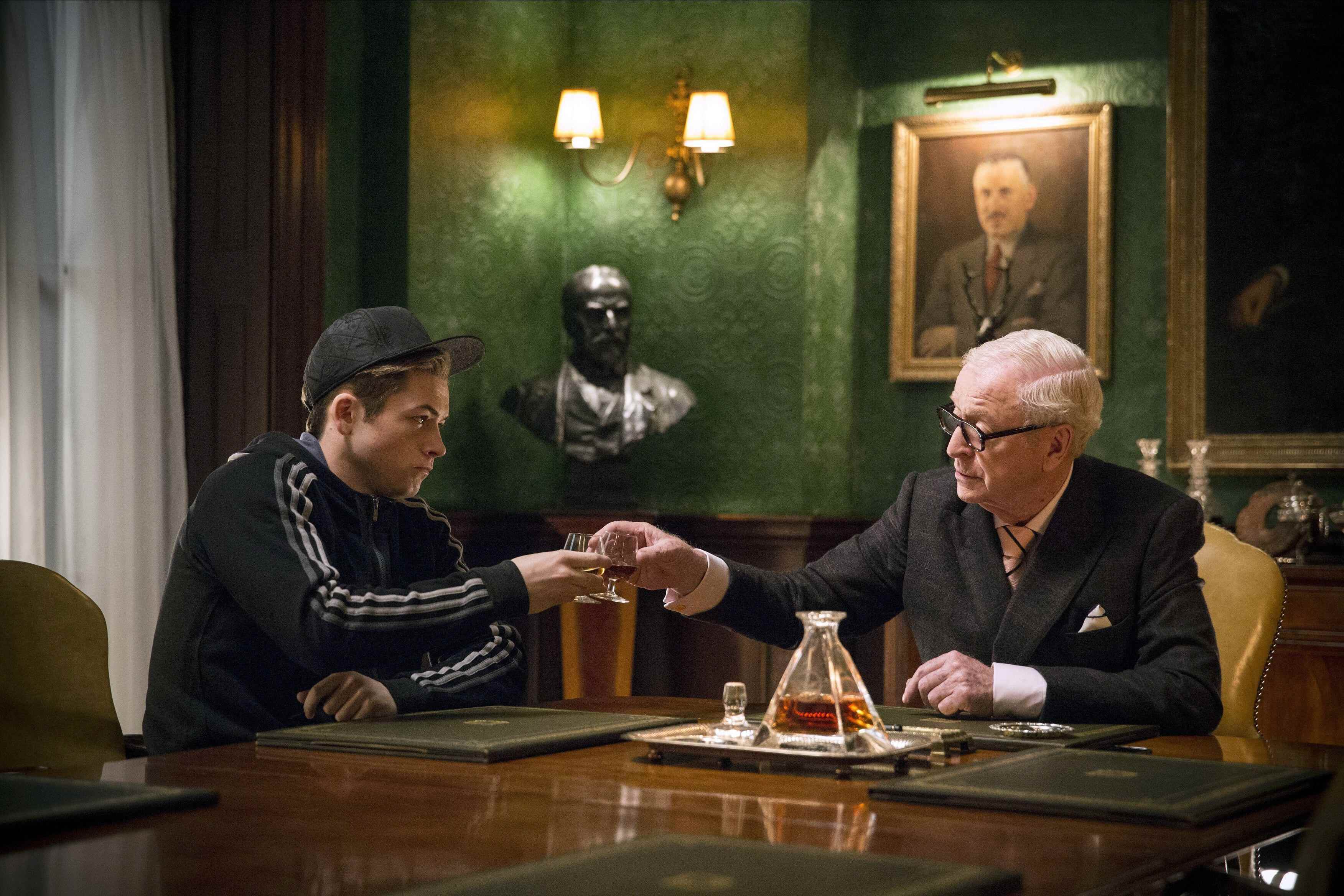 (Solda, Sağda) Eggsy rolünde Taron Egerton, Kingsman: The Secret Service'te Chester King rolündeki Michael Caine'e kadeh kaldırıyor