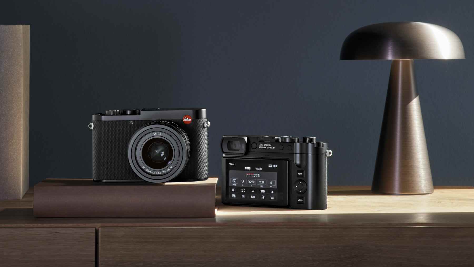 Ahşap masa üzerinde biri öne, diğeri uzağa bakan iki Leica Q3 kamera
