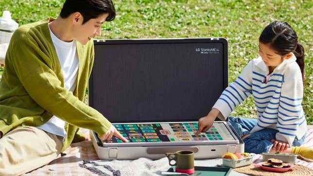 Bir parkta piknik yapan iki kişi ekranı düz bir şekilde dijital masa oyunu oynamak için LG StanbyME kullanarak.