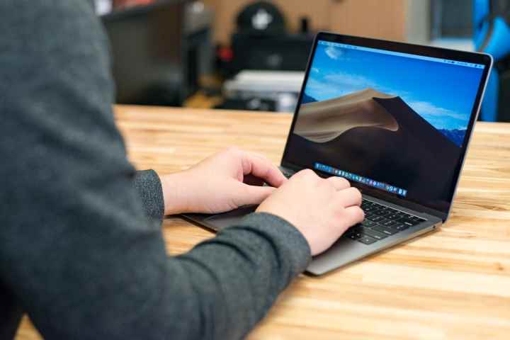 Ahşap bir masanın üzerinde duran bir 2018 Macbook Air'in üzerinde duran bir kişinin elleri.