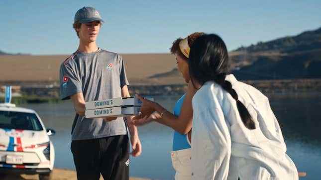 Bir Domino's kuryesi göl kenarında iki pizzayı iki kişiye teslim ediyor.
