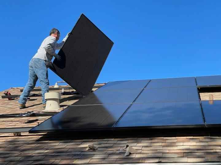 Bir evin çatısına güneş paneli kuran bir adam.