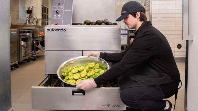 Bir Chipotle çalışanı, soyulmuş ve hazırlanmış dev bir kase avokado meyvesini Autocado makinesinden çıkarıyor.