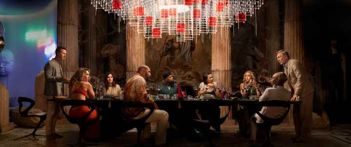 Glass Onion oyuncuları, Netflix filminden bir sahnede bir masanın etrafında toplanıyor.