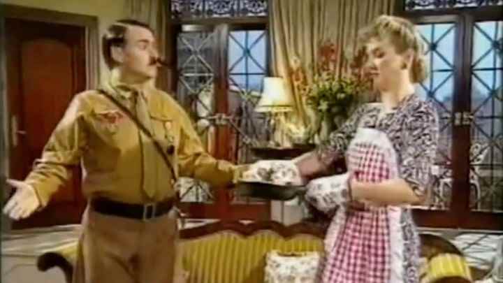 Heil Honey I'm Home! programında Hitler gibi giyinmiş bir aktör sitcom benzeri bir ev sahnesinde karısıyla konuşuyor.