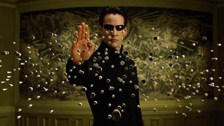 Matrix Reloaded'da Neo olarak Keanu Reeves, üzerine gelen düzinelerce mermiyi durduruyor.